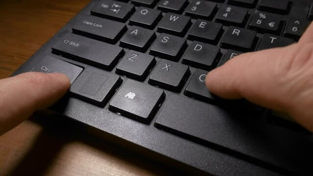 A black keyboard of a computer and a man's hands pressing the CTRL and C keys to do the copy, and then CTRL and V keys to do the paste command. Close up shot