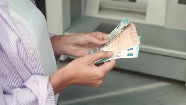 Extreme close-up of young woman withdrawing cash euro notes from ATM terminal. Caucasian female counting bills received from debit card standing on street. Financial operations concept.