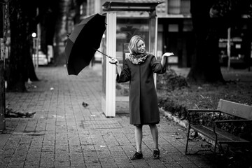 Obraz na płótnie Canvas A woman opens her umbrella outside checking for rain. Black and white photo.
