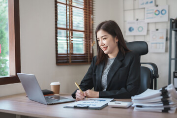 Fototapeta na wymiar Beautiful Asian businesswoman using her laptop enjoying work, taking notes, reviewing work done.