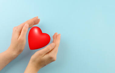 Red heart in woman hands on blue background. Copy space