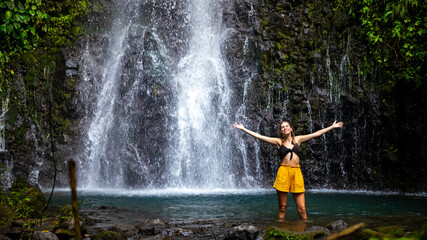 Obraz premium A beautiful girl spreads her arms while standing under a tropical waterfall in Costa Rica; swimming in a hidden waterfall in the rainforest; don jose waterfalls