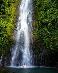 A relaxed man takes a refreshing bath under a tropical waterfall in Costa Rica; bathing at a hidden waterfall in the rainforest; don jose waterfalls