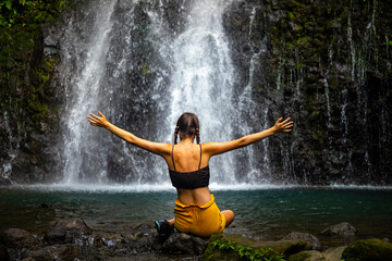A beautiful girl spreads her arms while standing under a tropical waterfall in Costa Rica; swimming in a hidden waterfall in the rainforest; don jose waterfalls