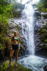 A beautiful girl spreads her arms while standing under a tropical waterfall in Costa Rica; swimming in a hidden waterfall in the rainforest