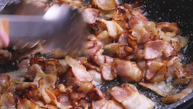 Crispy fried bacon in pieces lies in a heap in a frying pan