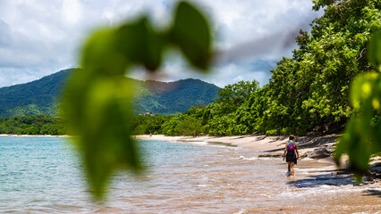 a beautiful girl in a short skirt walks on the famous conchal beach on the pacific coast of Costa Rica  a paradise beach with turquoise water and green hills in the background © Lens Down Under