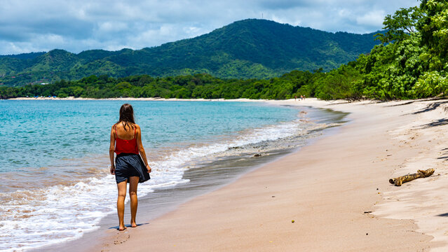 a beautiful girl in a short skirt walks on the famous conchal beach on the pacific coast of Costa Rica; a paradise beach with turquoise water and green hills in the background