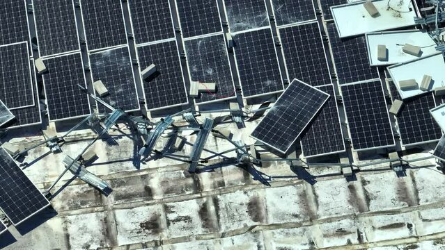 Aerial view of damaged by hurricane wind photovoltaic solar panels mounted on industrial building roof for producing green ecological electricity. Consequences of natural disaster