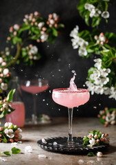 Spring and summer refreshing pink cocktail with apple blossom on light background. Pink summer cocktail