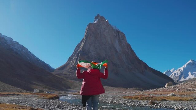 Rear view of Indian female hiker resting Indian flag on her shoulder while trekking on mountain at Zanskar, Ladakh, India. Girl waving Indian flag with pride. Concept of success or victory