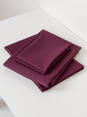 Maroon bed linen on white background. Stack of folded bed linen