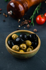 Green olives and black olives in a bowl on a dark background.