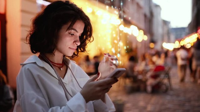 Beautiful Smiling Woman Using Phone on a City Street at Night. Smartphone Sending Data Up into the World Wide Connected Social Network