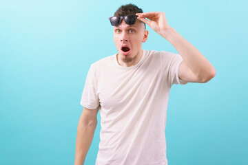 A very shocked man with an open mouth takes off black glasses on a blue background. Attractive. Crazy. Facial. Gesture. Surprised. Amazement. Shocked. Caucasian. Modern. Spectacle. Wonder. Amaze