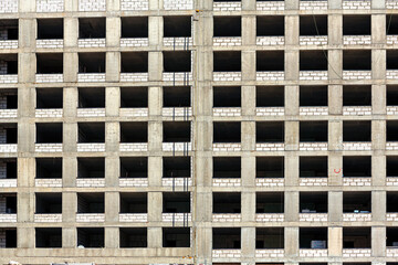 Monolithic concrete frame of apartment building under construction with partially attached facade cladding blocks.