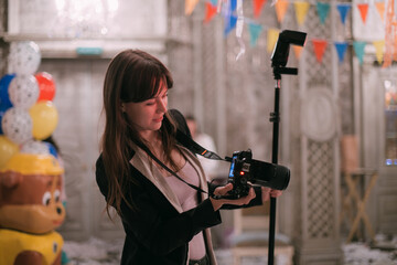 Girl photographer with a camera at work on the set in the banquet hall. A young beautiful woman - a professional photographer with a camera and a flash