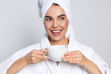 Young woman in bathrobe with towel and cup of drink on light grey background. Spa treatment