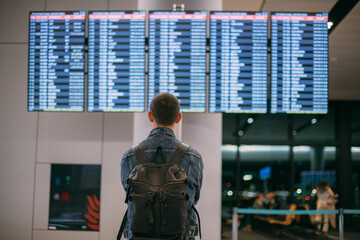 A male traveler with a backpack looks at the information board of departures and arrivals at the...