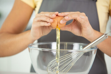 woman cracking egg open over glass bowl