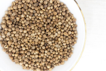 Pile of Coriander seeds in a white bowl on white wooden background