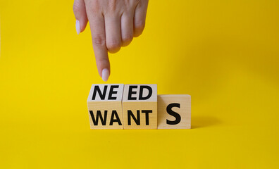 Needs and Wants symbol. Businessman Hand points at wooden cubes with words Wants and Needs. Beautiful yellow background. Business and Needs and Wants concept. Copy space