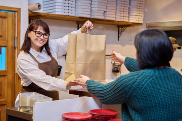 Woman restaurant worker issuing an order for takeaway food in paper bag