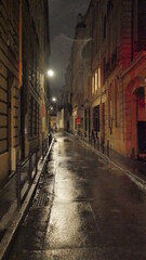 Sombre rue plongée dans la nuit, éclairé par des lampadaires nocturnes, mystérieux, obscur, peu de passant, passage de pluie, sol mouillé