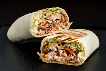 Fresh shawarma from chicken, tomatoes, lettuce, herbs, sauce and pita bread on a dark background. - 559575128