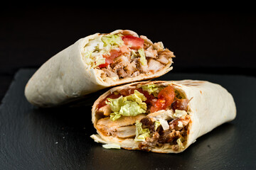 Shawarma from chicken, tomatoes, lettuce, herbs, sauce and pita bread on a dark background.