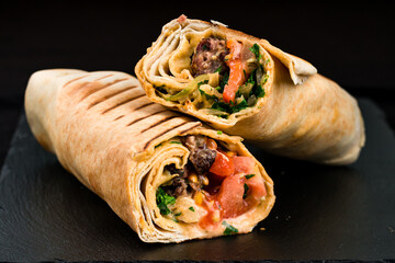 Shawarma from beef, tomatoes, greens, sauce and pita bread on a dark background.