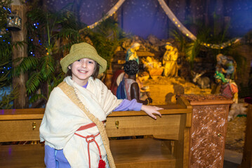 a boy actor dressed as a shepherd stands in front of the nativity scene in the church, waiting for...