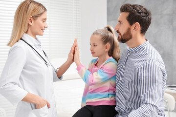 Happy father and daughter having appointment with doctor. Pediatrician and patient giving high five in clinic