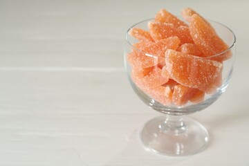 Tasty orange jelly candies in glass dessert bowl on white table. Space for text