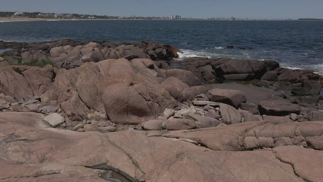 Rocas al borde del oceano donde se divisa a lo lejos ciudad turistica de veraneo 