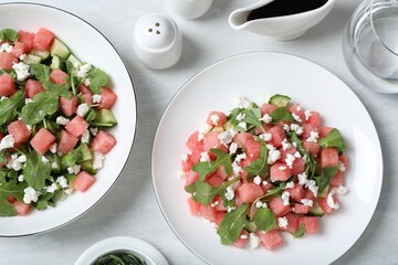 Delicious salad with watermelon, cucumber, arugula and feta cheese served on white wooden table, flat lay