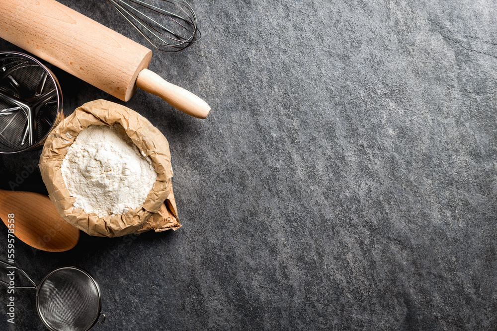 Poster Bakery background. Paper bag with flour, rolling pin and sieve on dark table with copy space top view
