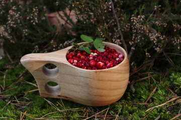 Many ripe lingonberries in wooden cup outdoors