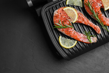 Cooking salmon. Grill with fresh fish steaks, lemon and rosemary on dark table, top view. Space for...