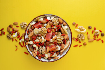 Bowl with mixed dried fruits and nuts on yellow background, flat lay