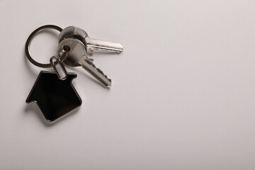 Keys with trinket in shape of house on white background, top view and space for text. Real estate agent services