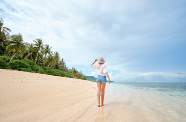Vacation on the seashore. Back view of young woman walking away on the beautiful tropical white sand beach. © Loginova