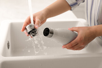 Woman washing thermo bottle in kitchen, closeup