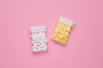 Containers with different dragee candies on pink background, flat lay