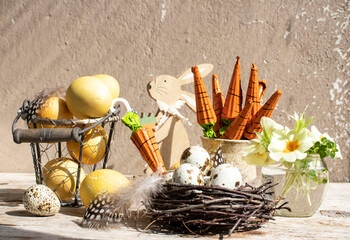 Easter still life. Colored eggs, carrot-shaped sweets, wooden figurines of rabbits, spring flowers.