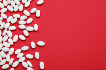 Fototapeta na wymiar Many white dragee candies on red background, flat lay. Space for text