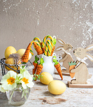 Easter still life. Colored eggs, carrot-shaped sweets, wooden figurines of rabbits, spring flowers.