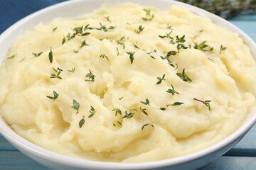 Bowl of tasty mashed potato with rosemary on light blue wooden table, closeup
