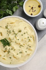 Bowl of tasty mashed potato, parsley, olive oil and pepper on grey marble table, flat lay