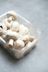 Champignon mushrooms in the plastic box at the grey background